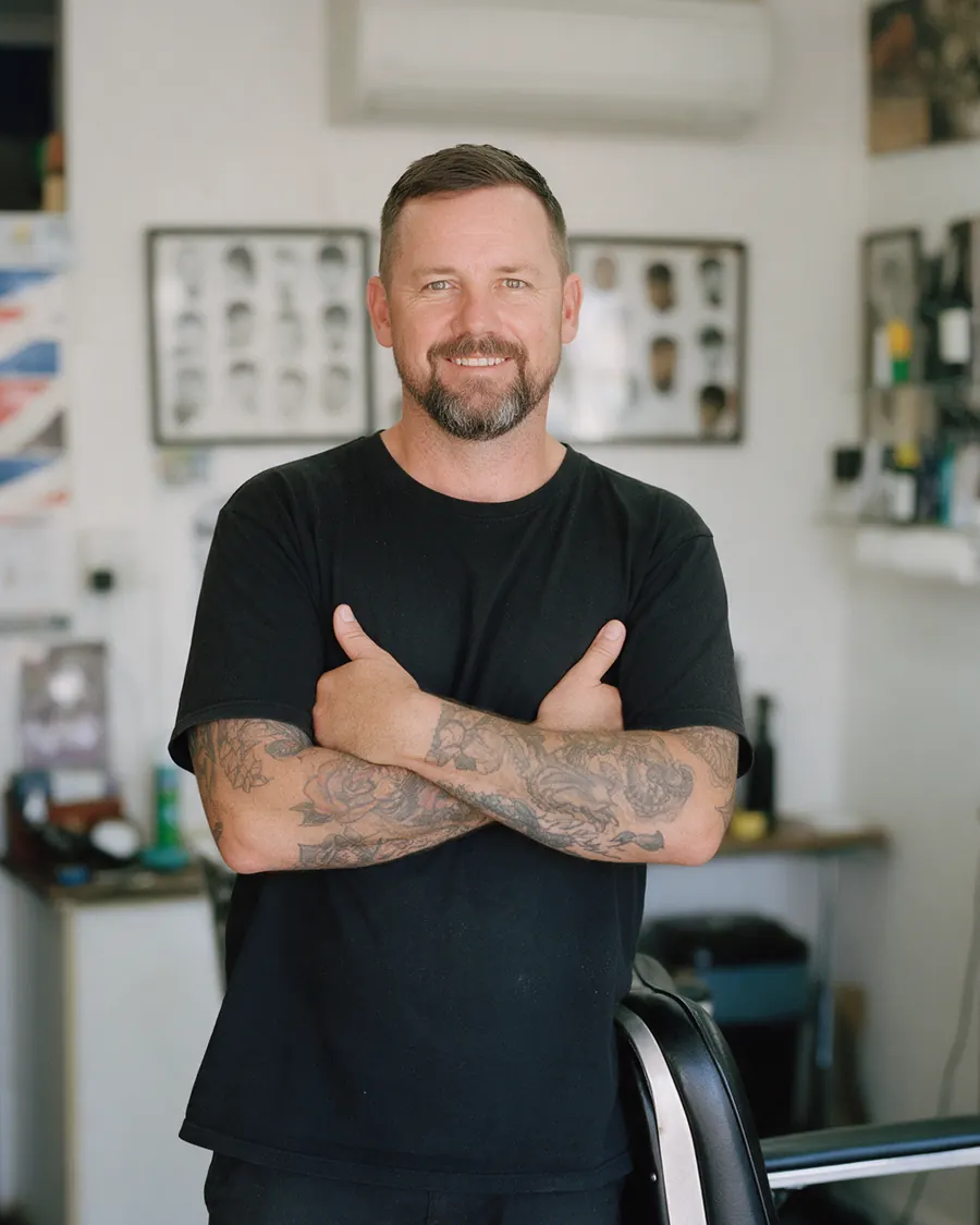 Ray Holloway, arms folded, beside his barber chair